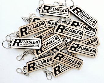 May include: A pile of wooden keychains with a silver metal ring. Each keychain has the text "Reliable Oilfield Hauling Ltd." printed in black.