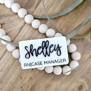 May include: White name tag with black text. The name tag says "Shelley RN|CASE MANAGER".