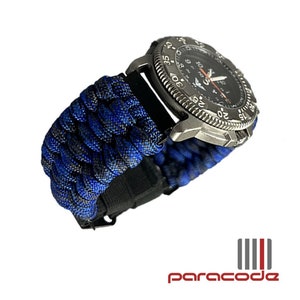 Puede incluir: Una correa de reloj de paracord negra y azul con una esfera de reloj plateada. La esfera del reloj tiene un fondo negro con números blancos y un bisel plateado con números blancos.