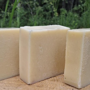 May include: Three rectangular bars of solid, off-white soap arranged in a row. Each bar features a smooth, matte surface with subtle variations in texture and color, showcasing a clean, uniform appearance without any added patterns or labels.