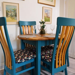 May include: A teal dining table with four chairs. The chairs have wooden backs and floral patterned cushions. The table has a wooden top and is set with two place settings.