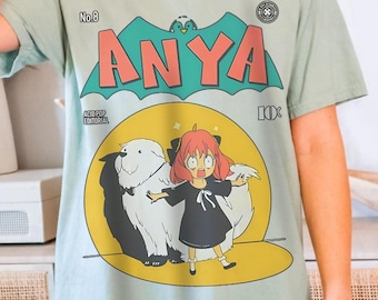 May include: A light blue t-shirt with a vintage comic book design featuring a girl named Anya with a dog. The comic book cover has a yellow background with a green bat and the text "Anya" in red and white.