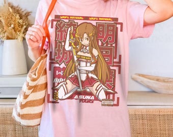 Może przedstawiać: Jasnoróżowa koszulka z grafiką postaci z anime trzymającej miecz. Grafika zawiera japoński i angielski tekst, w tym "NOT YOUR WAIFU" i "ASUNA YOURS".