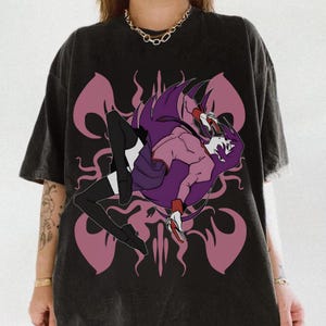 May include: Black t-shirt featuring a stylized anime-style illustration of a person with long purple hair and a pink outfit. The graphic is set against a backdrop of pink, abstract shapes. The shirt has a vintage, worn look.