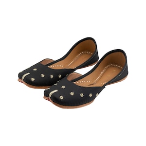 May include: A pair of black embroidered flat shoes with gold floral designs. The shoes have a pointed toe and a low heel.
