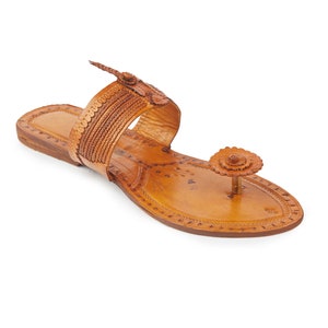 May include: A pair of brown leather sandals with intricate floral designs and a decorative flower embellishment on the toe strap.