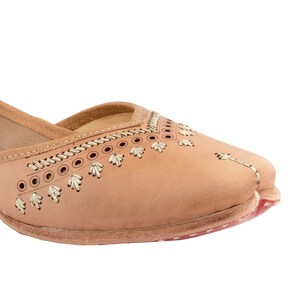 May include: Tan leather flat shoes with gold embroidery and stitching. The shoes have a pointed toe and a low heel.