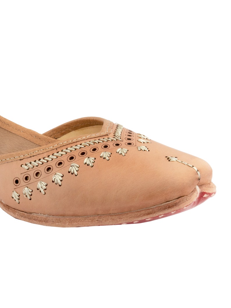 May include: Tan leather flat shoes with gold embroidery and stitching. The shoes have a pointed toe and a low heel.