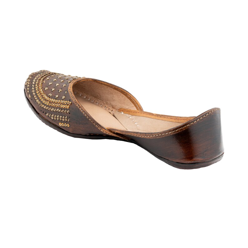 May include: Brown leather flat shoes with gold embellishments. The shoes have a pointed toe and a low heel.