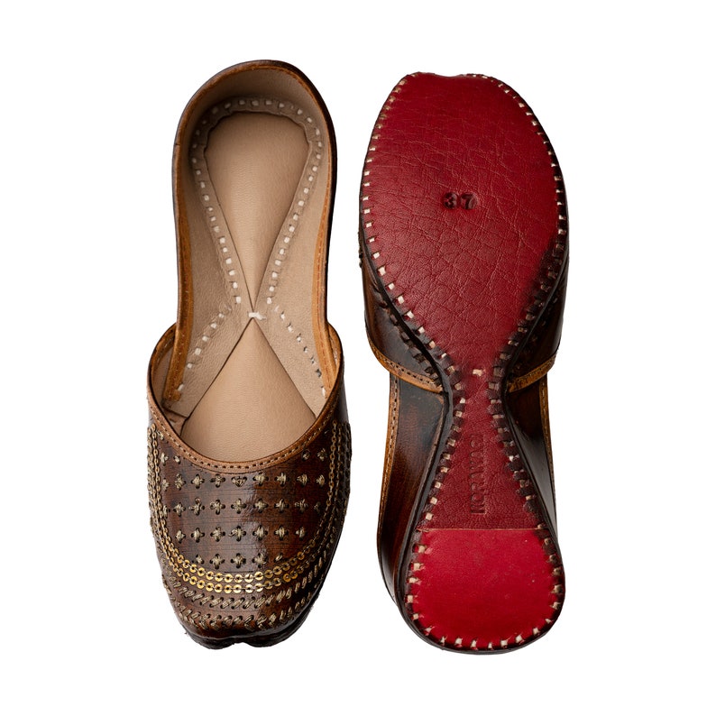 May include: A pair of brown leather shoes with gold embellishments. The shoes have a pointed toe and a low heel. The soles of the shoes are red.