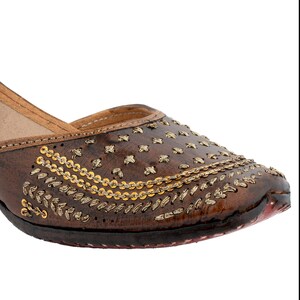 May include: Brown leather flat shoes with gold embroidery and embellishments.