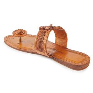 May include: Tan leather sandals with a decorative flower design on the toe strap and a braided strap across the foot.