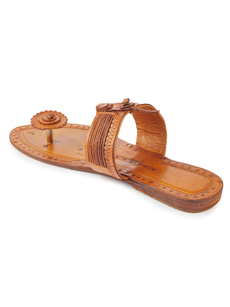 May include: Tan leather sandals with a decorative flower design on the toe strap and a braided strap across the foot.