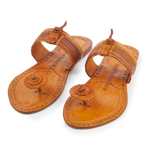 May include: A pair of brown leather sandals with intricate floral designs and a decorative button on the toe strap.