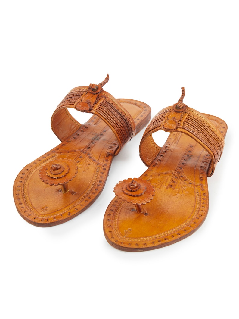 May include: A pair of brown leather sandals with intricate floral designs and a decorative button on the toe strap.