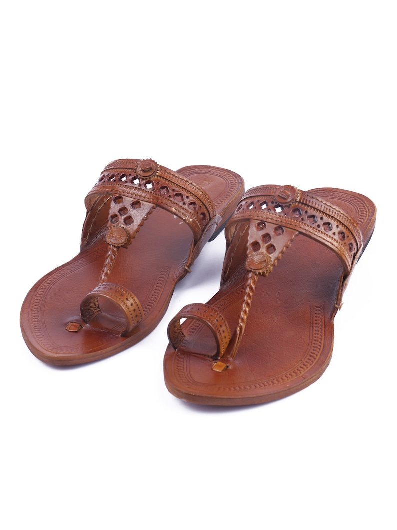 Pu&ograve; includere: Un paio di sandali in pelle marrone con design a passante per le dita. I sandali presentano ritagli decorativi sui cinturini e una suola strutturata. Le calzature sono progettate per un uso casual.