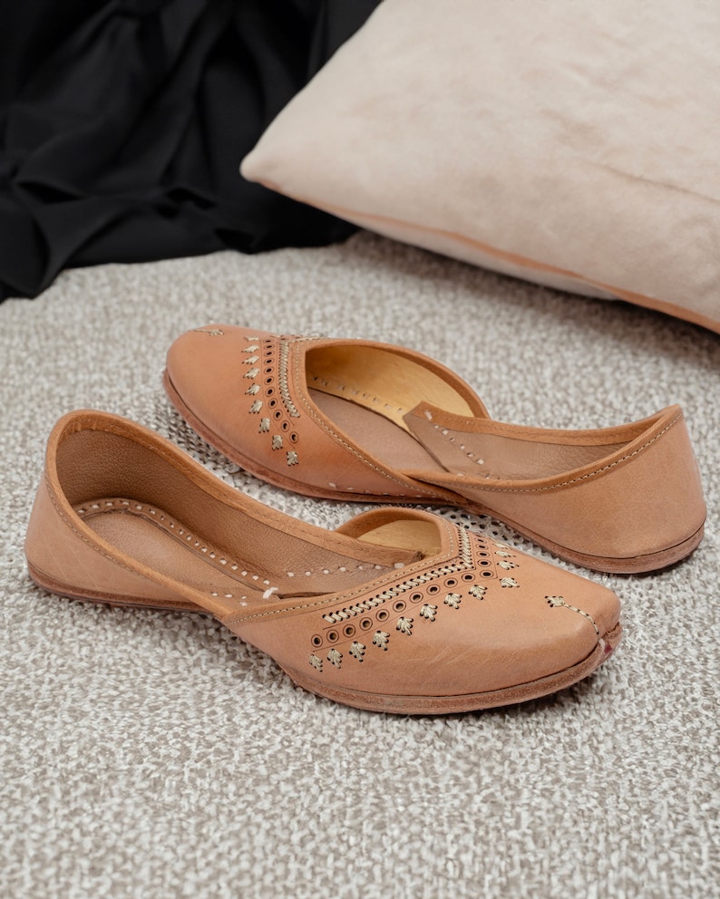 May include: A pair of tan leather shoes with intricate cut-out designs and gold embellishments. The shoes have a pointed toe and a low heel.