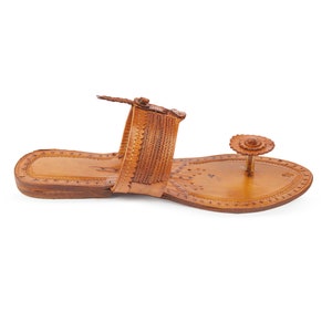 May include: A pair of brown leather sandals with intricate floral designs and a decorative flower embellishment on the toe strap.