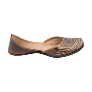 May include: Brown leather flat shoes with gold embellishments. The shoes have a pointed toe and a low heel.