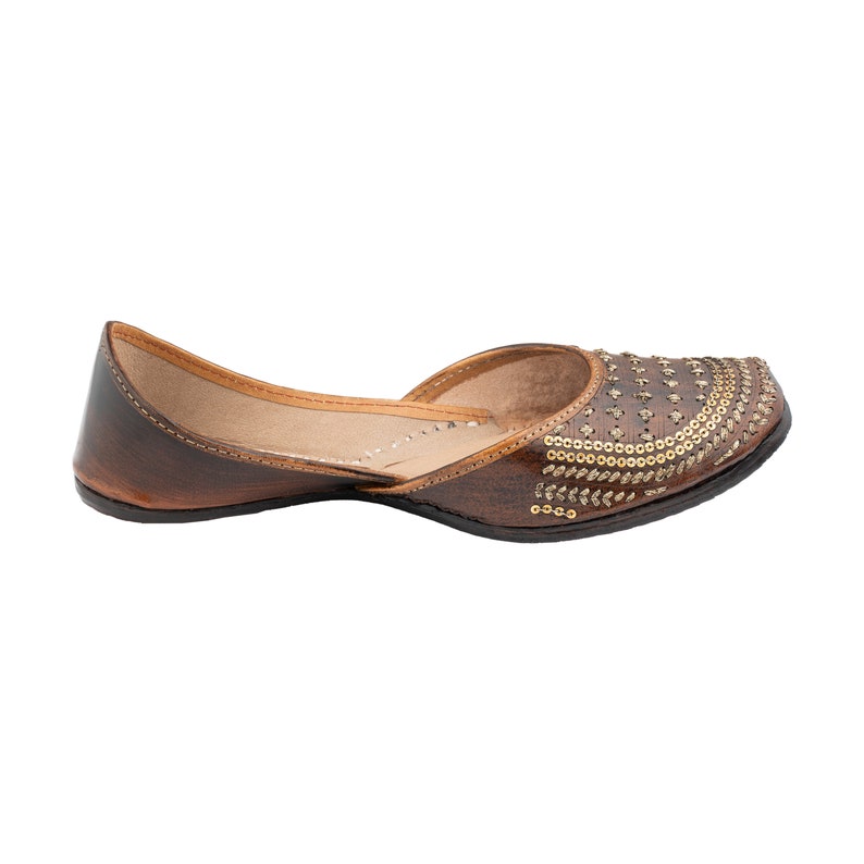 May include: Brown leather flat shoes with gold embellishments. The shoes have a pointed toe and a low heel.