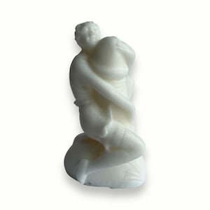 Op de afbeelding: Witte keramische sculptuur van twee figuren die elkaar omhelzen. De figuren zitten en lijken in elkaar verstrengeld te zijn.