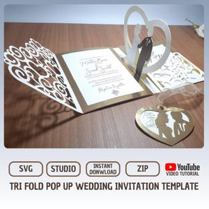 May include: A tri-fold pop-up wedding invitation template. The invitation is open, revealing the names "Mattin B" and "Sarah Smith" on a white card with gold trim. A heart-shaped cutout with a bride and groom figure is visible. The invitation has decorative cutouts and a heart-shaped tag.