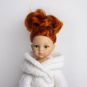 May include: A red-haired doll wearing a white bathrobe. The doll has green eyes and a light complexion.