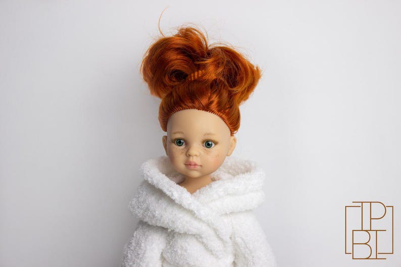 May include: A red-haired doll wearing a white bathrobe. The doll has green eyes and a light complexion.