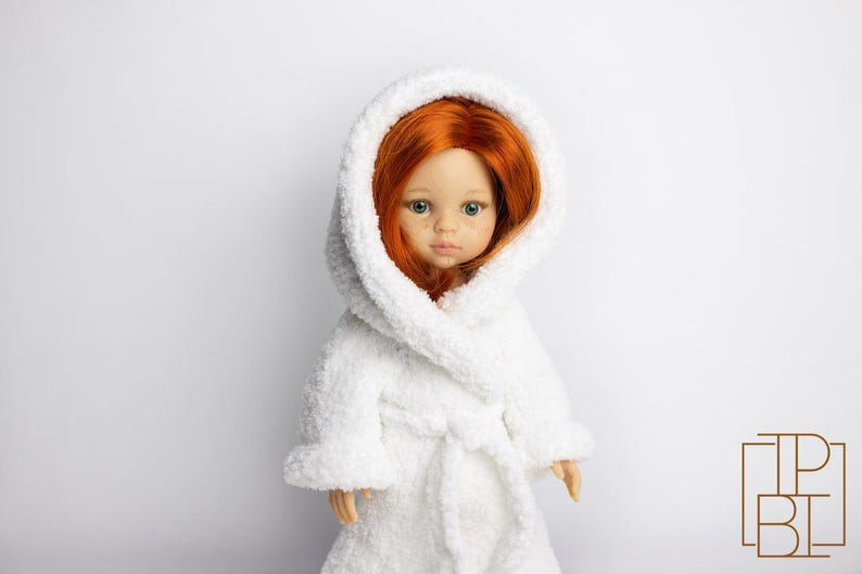 May include: A white plush bathrobe with a hood, worn by a doll with long red hair and blue eyes.