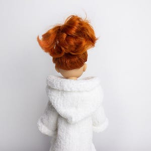 May include: A white hooded robe with a soft, fluffy texture. The robe is worn by a doll with long, red hair pulled back in a ponytail.