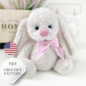 May include: A white crocheted bunny with pink ears and a pink and white striped bow. The bunny has blue eyes and a pink nose. The bunny is sitting on a white surface. PDF Crochet Pattern.