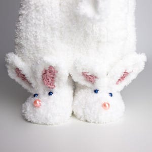 May include: White fuzzy bunny slippers with pink ears and blue eyes. The slippers have a fluffy texture and are perfect for keeping your feet warm.