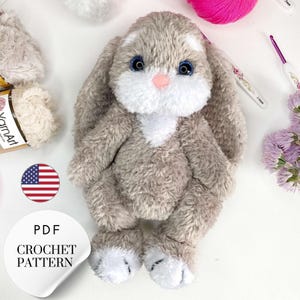 May include: A crochet pattern for a plush bunny toy. The bunny is gray with white accents and blue eyes. The pattern is available as a PDF download.