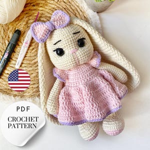 Peut inclure: Un patron de crochet pour un lapin rose et blanc portant une robe rose avec un nœud violet. Le patron est disponible en téléchargement PDF.