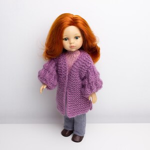 Pode incluir: Uma boneca com cabelo comprido e ruivo vestindo um casaco de tric&ocirc; roxo e cal&ccedil;as cinzas. A boneca est&aacute; em p&eacute; em um fundo branco.