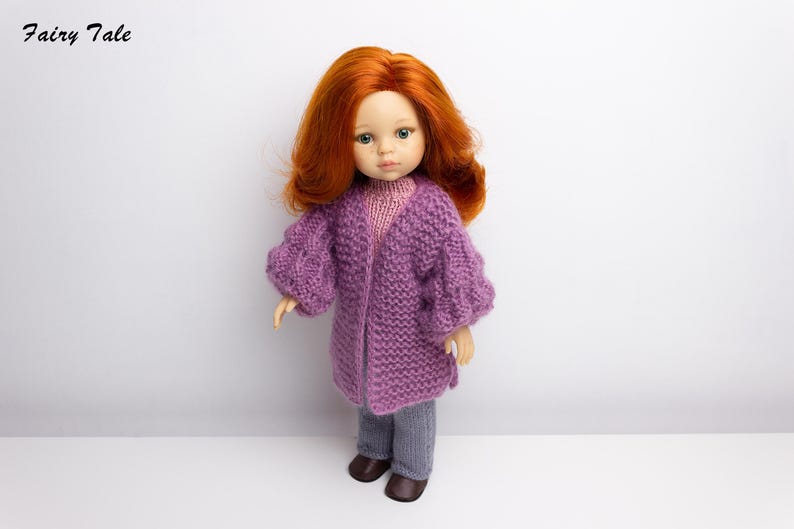 Pode incluir: Uma boneca com cabelo comprido e ruivo vestindo um casaco de tric&ocirc; roxo e cal&ccedil;as cinzas. A boneca est&aacute; em p&eacute; em um fundo branco.
