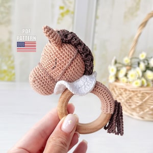 Può includere: Giocattolo sonaglio a forma di testa di cavallo lavorato a uncinetto con un anello di legno. Il cavallo è marrone e beige con un colletto a volant bianco e una criniera marrone. Il giocattolo è perfetto per il primo giocattolo di un bambino.