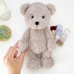 Pu&ograve; includere: Un orsacchiotto di peluche marrone chiaro con occhi neri e un naso nero. L'orso &egrave; in piedi su una superficie bianca.
