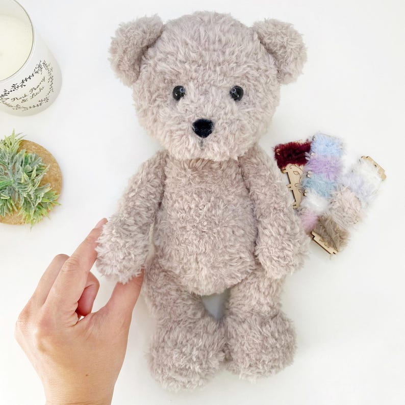Pu&ograve; includere: Un orsacchiotto di peluche marrone chiaro con occhi neri e un naso nero. L'orso &egrave; in piedi su una superficie bianca.
