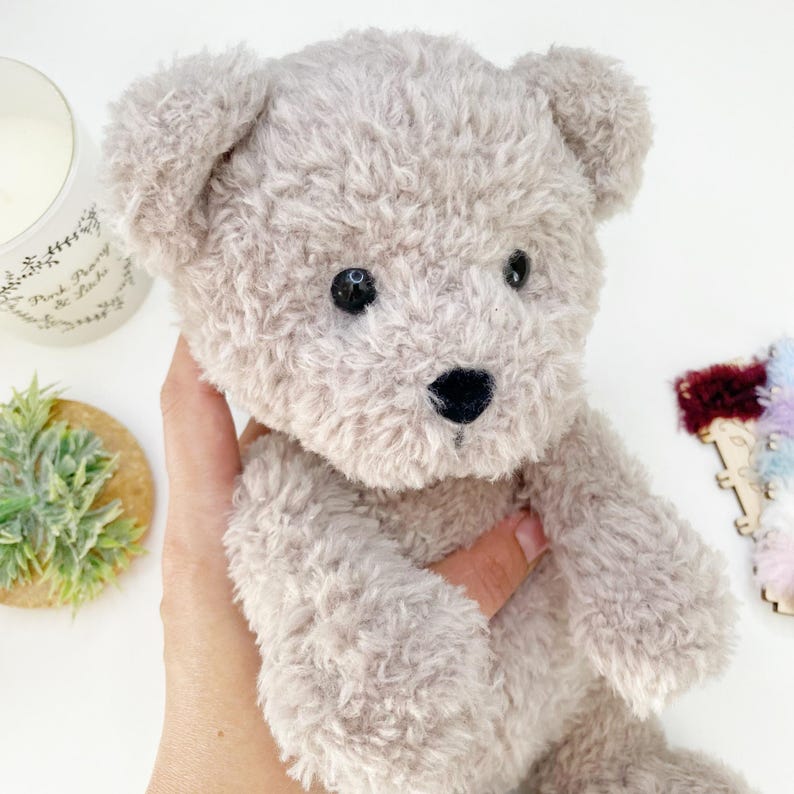 Pu&ograve; includere: Un orsacchiotto di peluche morbido e soffice con una pelliccia marrone chiaro. L'orso ha occhi neri e un naso nero. L'orso &egrave; tenuto da una mano.