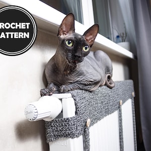 Könnte beinhalten: Ein grauer Häkel-Heizkörperbezug mit Knöpfen, einem weißen Thermostat und einer schwarzen haarlosen Katze, die darauf sitzt. Der Text "CROCHET PATTERN" befindet sich in einem schwarzen Kreis an der Wand.