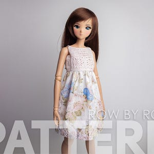 May include: A doll wearing a white crochet top with a floral print skirt. The doll has long brown hair and blue eyes.