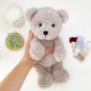 Pu&ograve; includere: Un orsacchiotto di peluche morbido e soffice di colore marrone chiaro con occhi neri e naso nero. L'orso &egrave; seduto dritto con le braccia e le gambe leggermente piegate.
