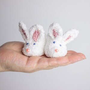 May include: A pair of white bunny-shaped baby booties with pink ears and blue eyes.