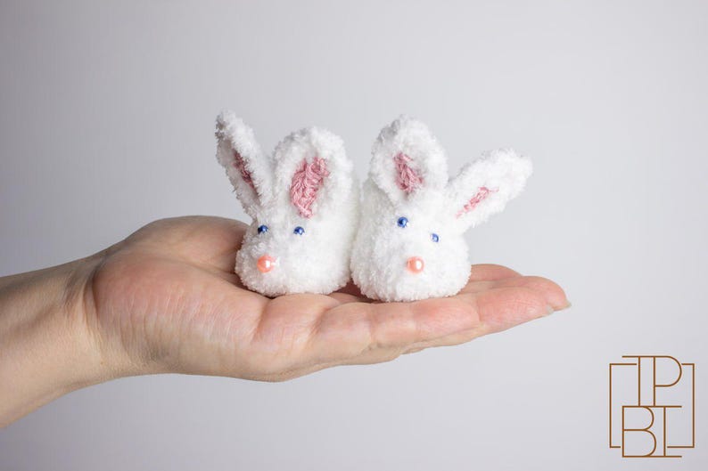 May include: A pair of white bunny-shaped baby booties with pink ears and blue eyes.