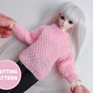 May include: A pink knitted sweater on a doll with long white hair. The sweater has long sleeves and a crew neck. The doll is wearing black pants. A pink circle with the words "KNITTING PATTERN" is in the lower left corner.
