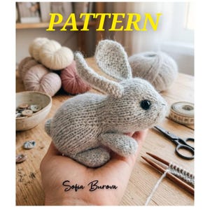 May include: A knitted grey bunny toy with black eyes and long ears. The word "PATTERN" is in yellow text above the bunny. The bunny is held in a hand, with knitting supplies and yarn in the background. The name "Sofia Burova" is written below the bunny.