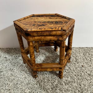 May include: A hexagonal stool constructed from natural bamboo with a mottled brown finish. The piece features a flat, six-sided top surface supported by six vertical bamboo legs connected by horizontal bamboo crossbars near the base.