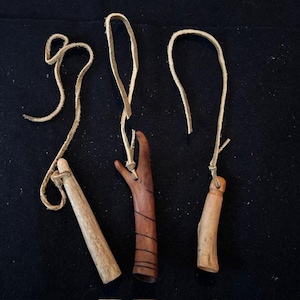 May include: Three handcrafted wooden pendants with leather cords. One is light brown, cylindrical, and another is a darker brown with carved lines. The third is a light brown, with a rounded shape. All have leather cords.