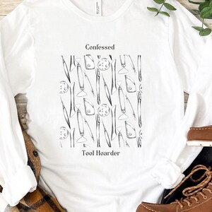 May include: White long-sleeved t-shirt with a black and white graphic of tools and the text "Confessed Tool Hoarder".